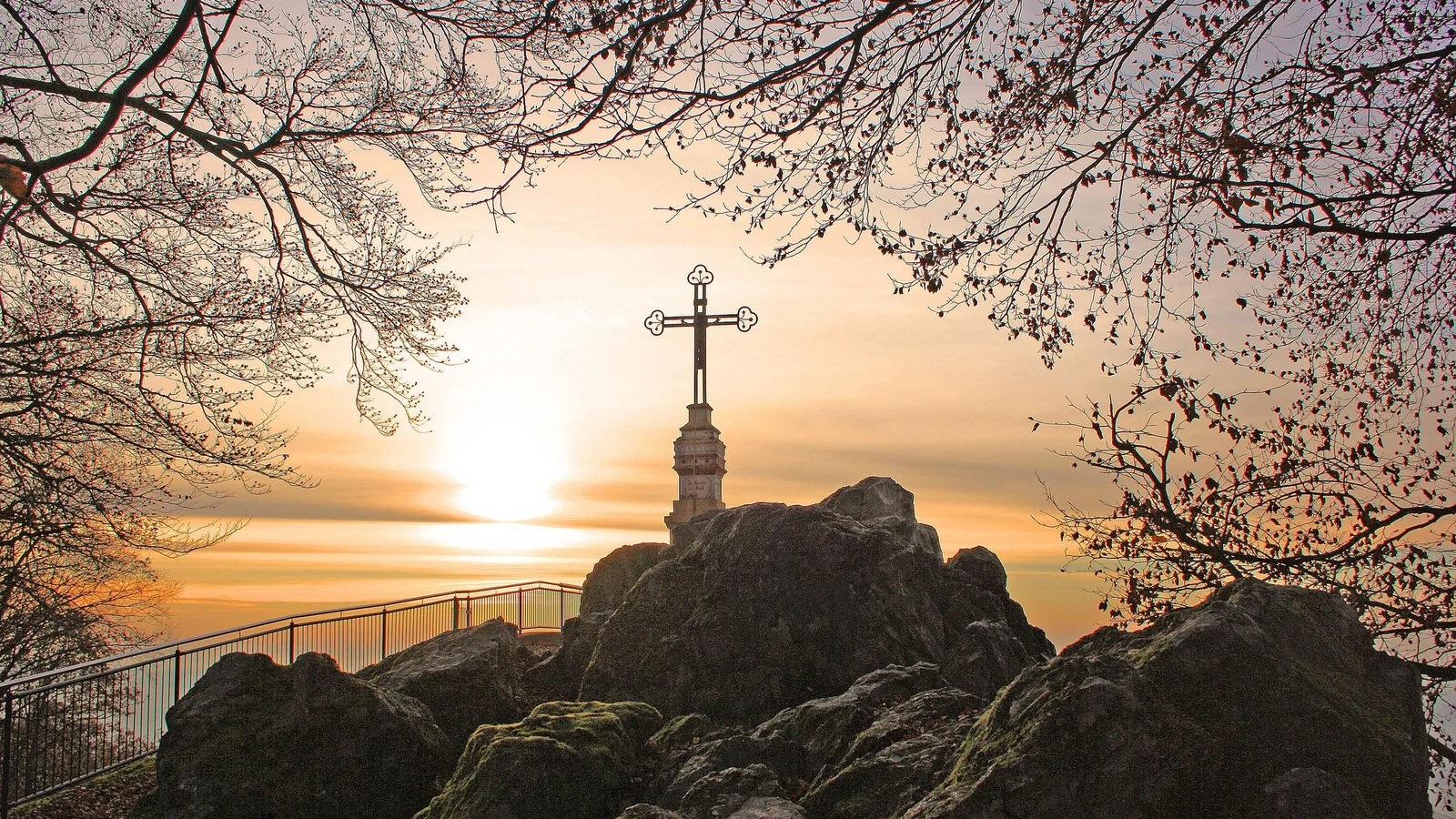 A cross stands on a rocky hill at sunrise.
