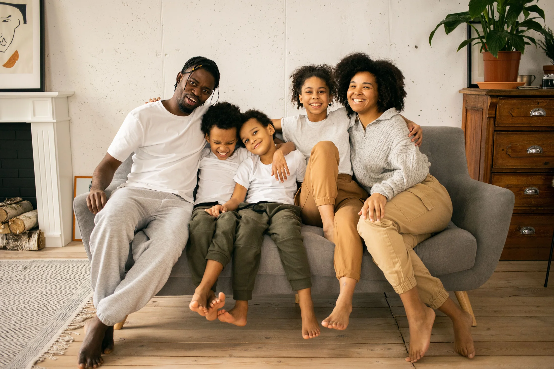 A Black family of five sitting closely together on a sofa at home